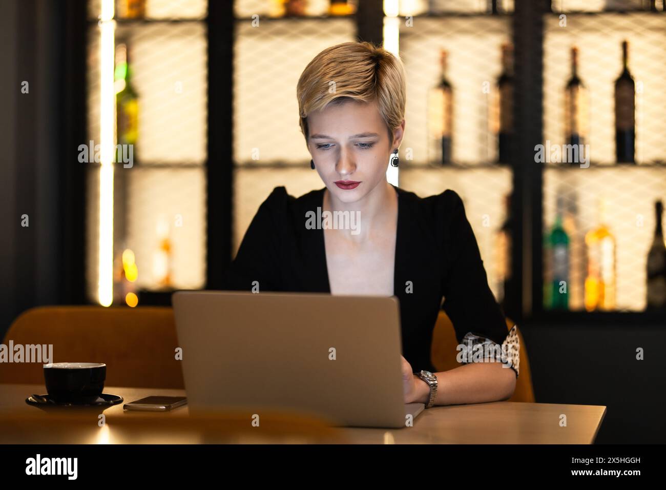 A professional young woman concentrates on her work on a laptop in a cozy café environment, displaying focus and determination. Stock Photo