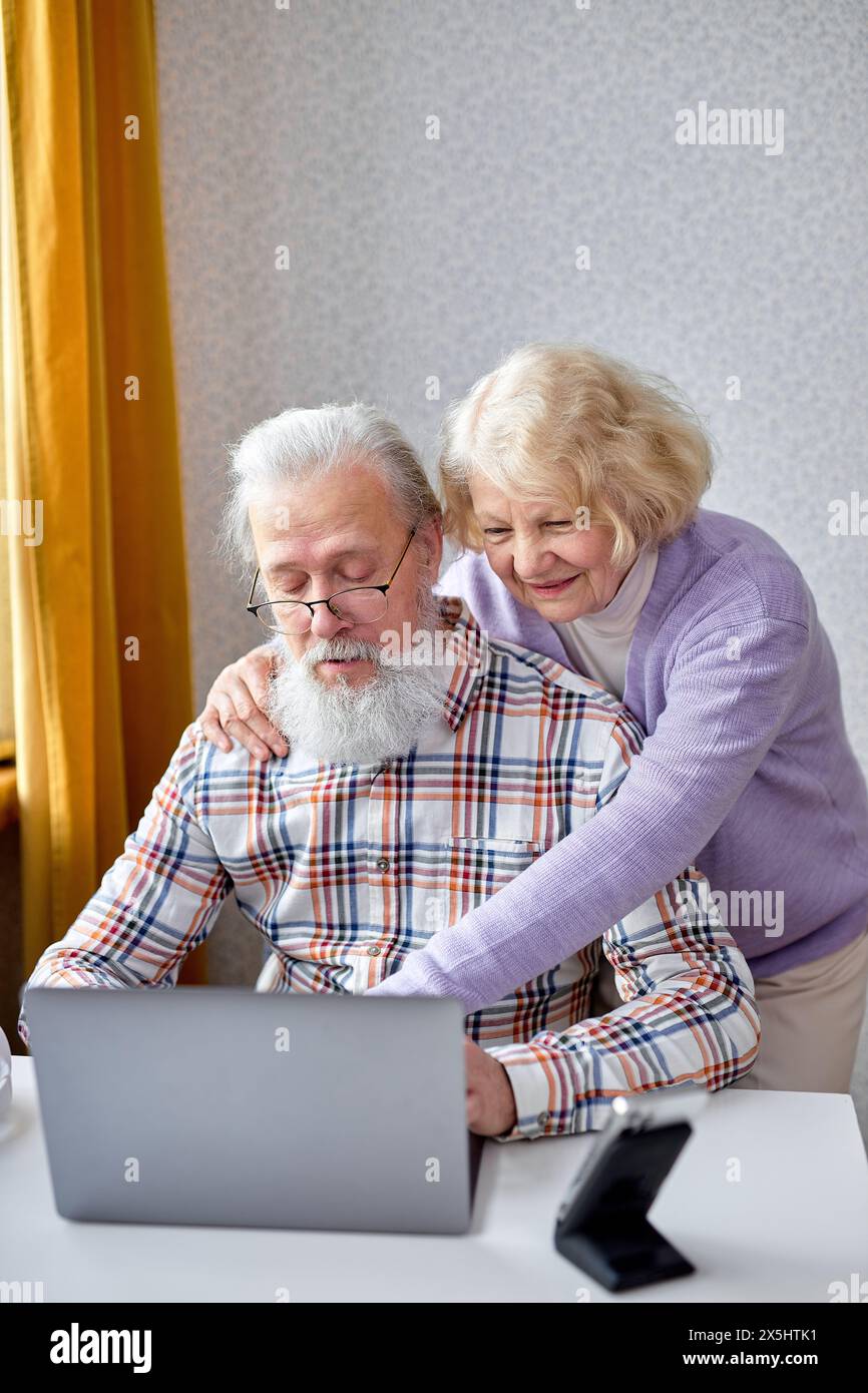 Old spouses using apps on laptop. Happy elderly couple having fun online, surfing the Net. Senior people active social networks users spend time together, watching something interesting Stock Photo