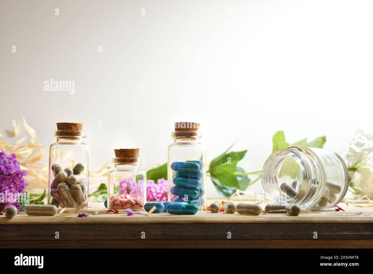 Natural laboratory medications with capsules and pills in glass bottles with plants and flowers on wooden table and white isolated background. Front v Stock Photo