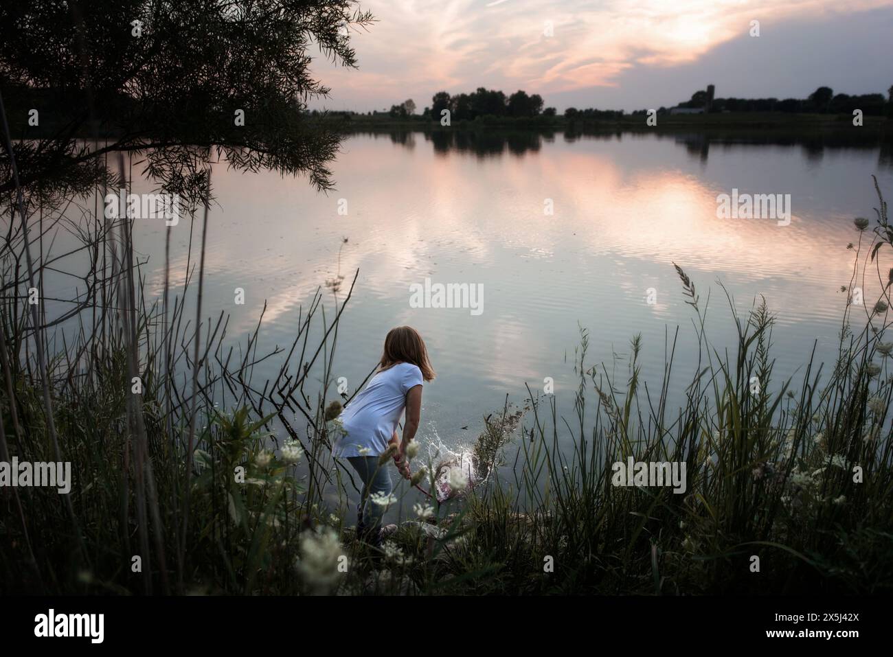 Young girl splashing water in beautiful lake at sunset Stock Photo