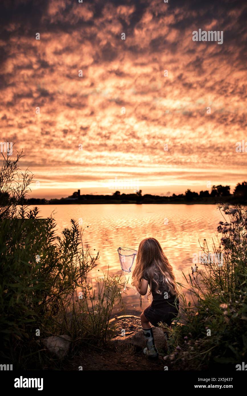 Young girl fishing at gorgeous lake at sunset Stock Photo