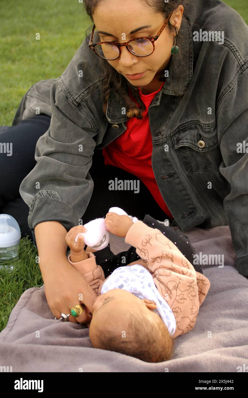 Attentive mother interacts closely with baby on park blanket Stock Photo