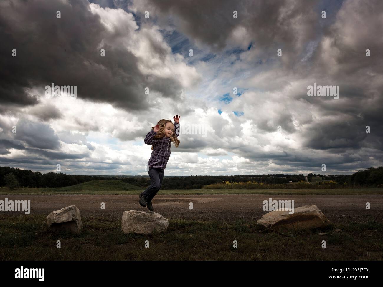 Little girl jumping on rocks under stormy sky Stock Photo - Alamy