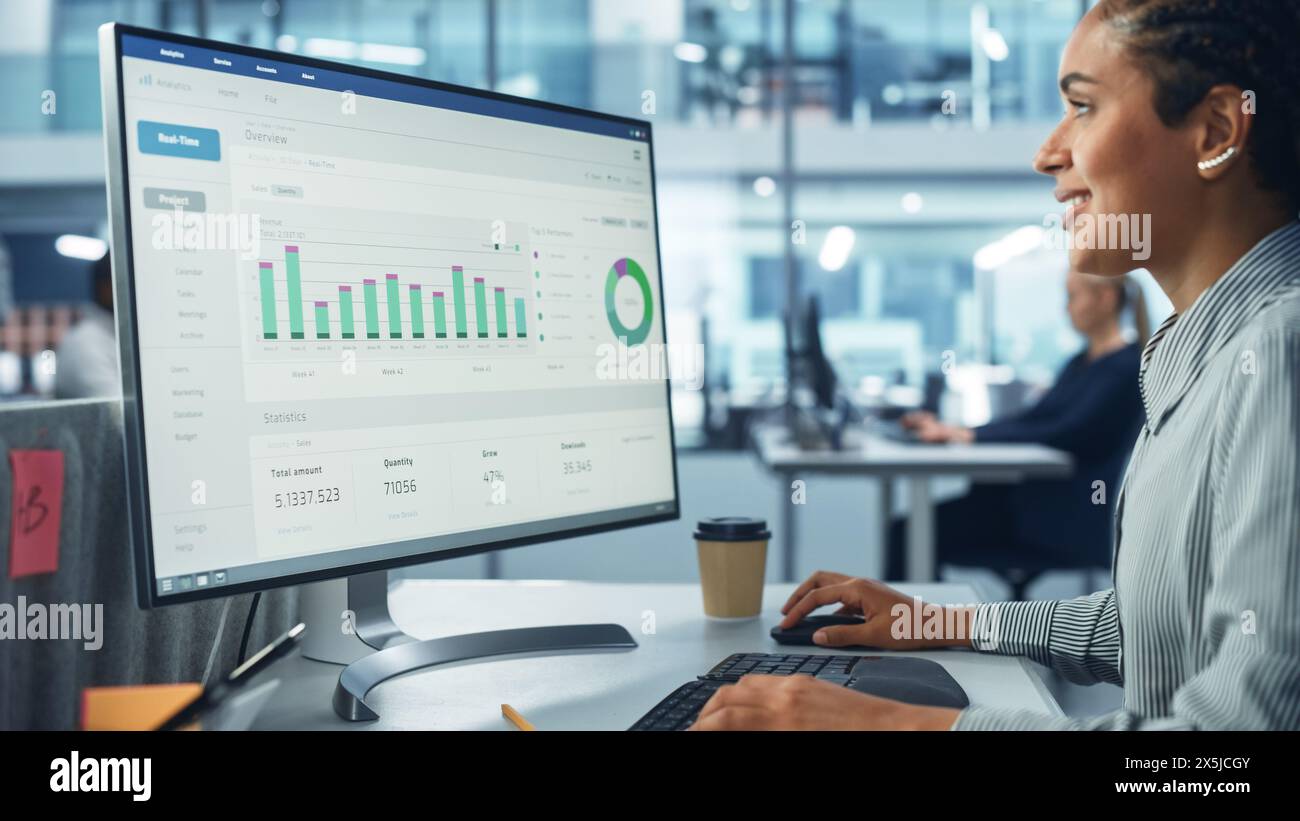 Corporate Office: Black Female IT Technician Using Desktop Computer with Big Data Statistics, Graphs. Smiling Creative Software Engineer Work on eCommerce Project Marketing, Development. Stock Photo