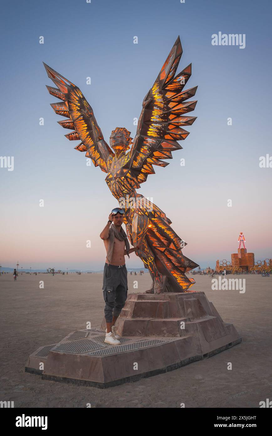 Man near illuminated angel sculpture in desert at dusk Stock Photo