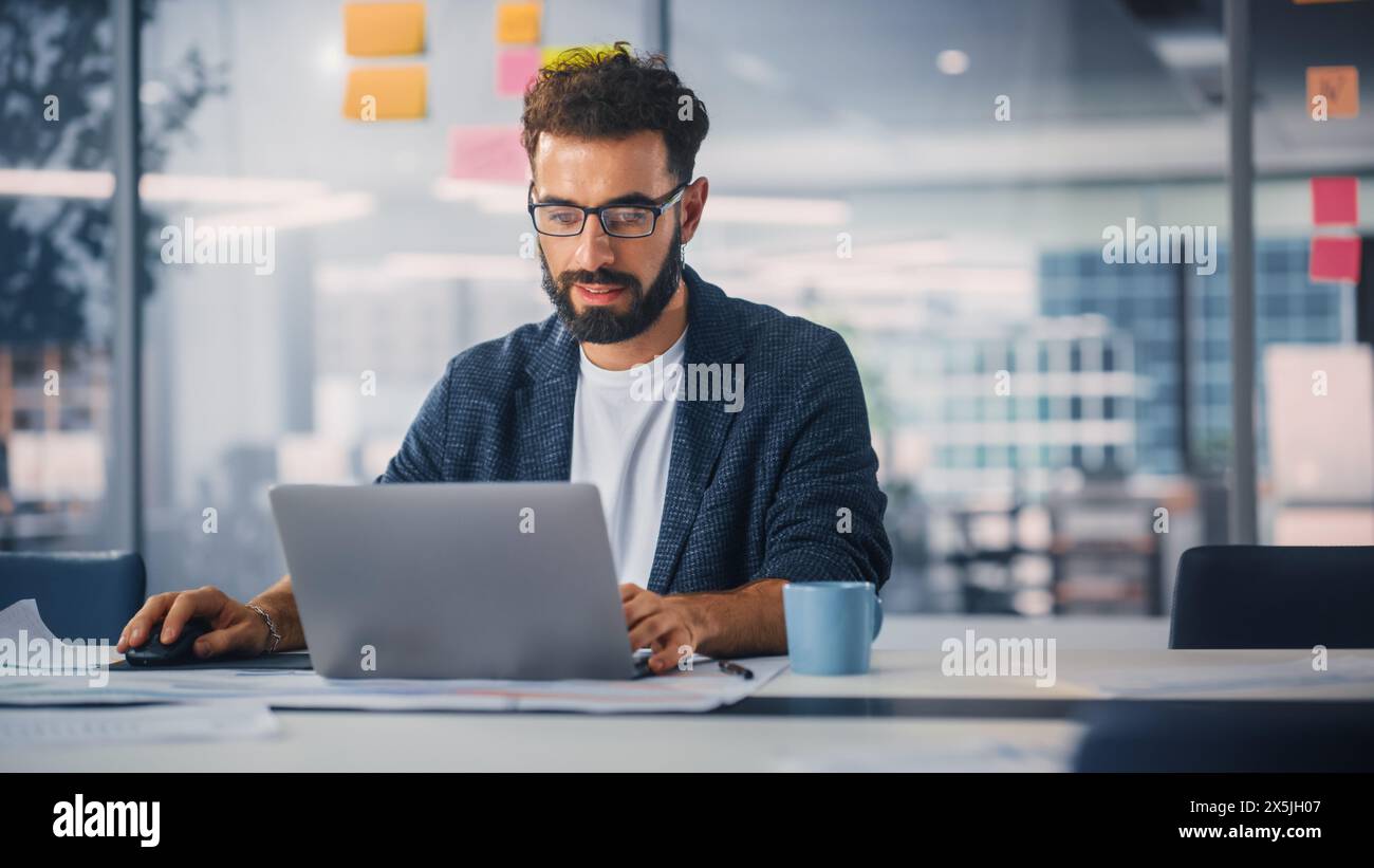 Modern Office: Portrait of Young Stylish Businessman Wearing Glasses Works on Laptop, Does Data Analysis, Website Design, Creative Developemnt. Digital Entrepreneur Works on e-Commerce Startup Project Stock Photo