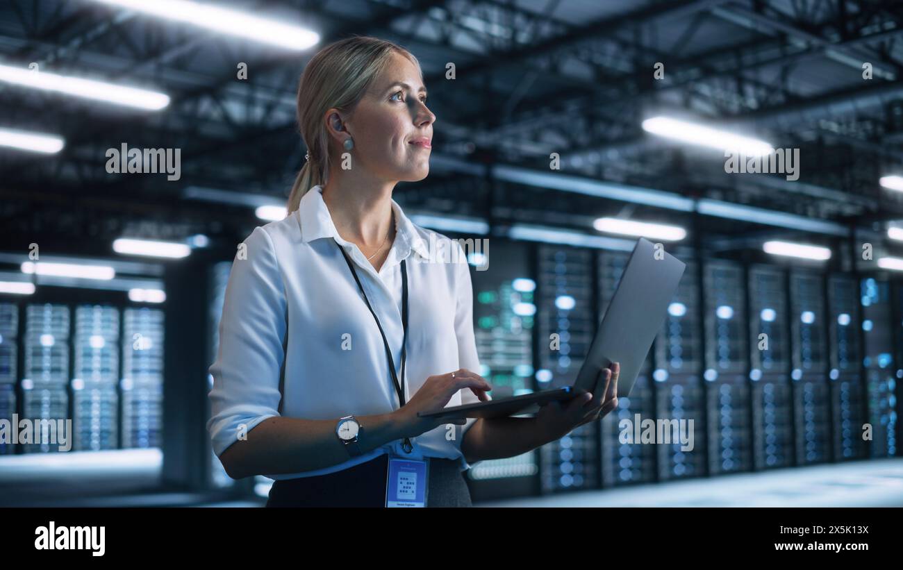 Female Engineer Holding Laptop Computer at Hands while Programs Something. She Works in Modern High-Tech Office. High-Speed Data Transfer and Smooth Server Operation, Analytics, Statistics Concept Stock Photo