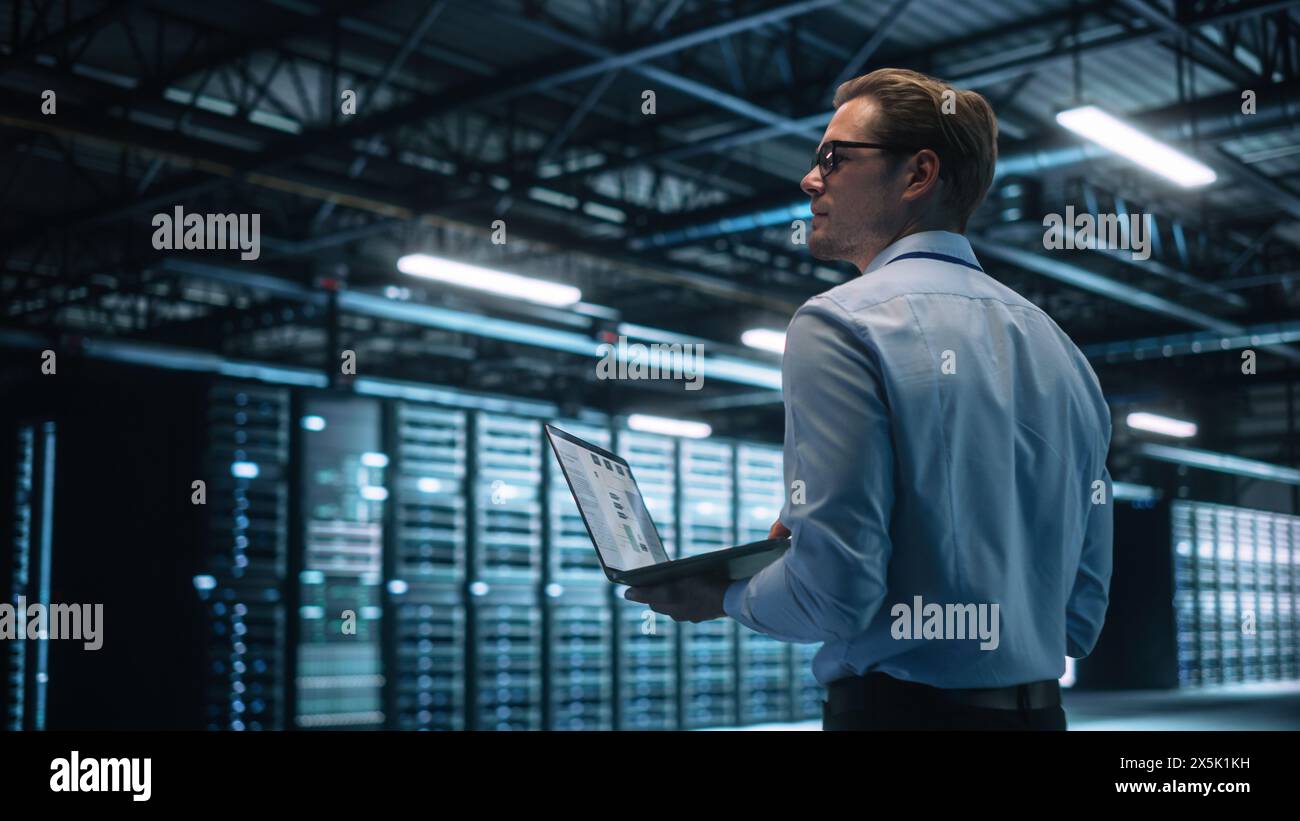 Creative Caucasian Man Using a Laptop Computer in Evening Office. Independent Businessman is Walking Through the Office and Looking Away. Technology Science Breakethrough, Progress, Innovation Concept Stock Photo