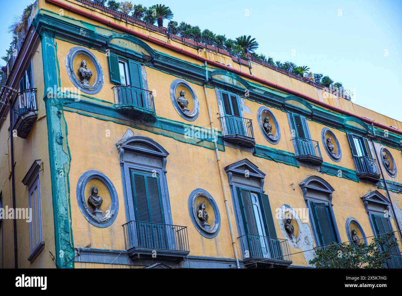 Naples, Italy. Mediterranean yellow building with green-blue balconies, shutters and statues Stock Photo