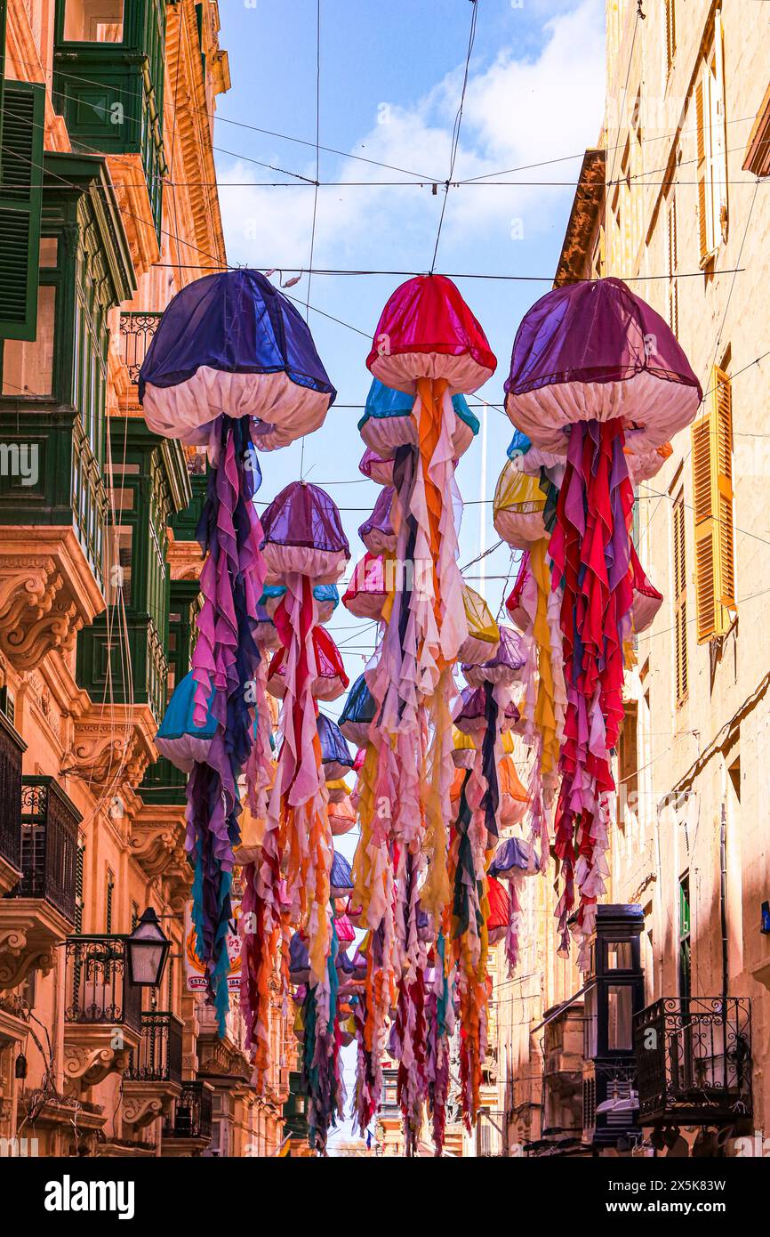 Valletta, Malta. Cascading down a street are colorful parachute jellyfish and green balconies Stock Photo