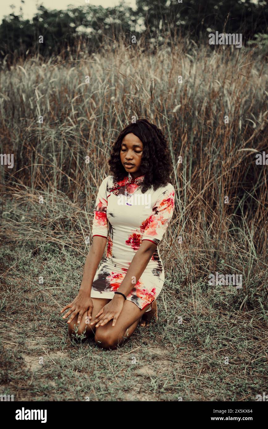 Nigeria, Delta state, Woman in mini dress kneeling in field Stock Photo