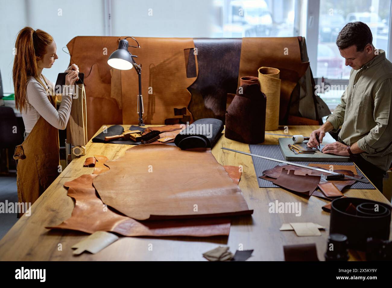 ginger woman in apron using stitching clamp at work, her colleague ...