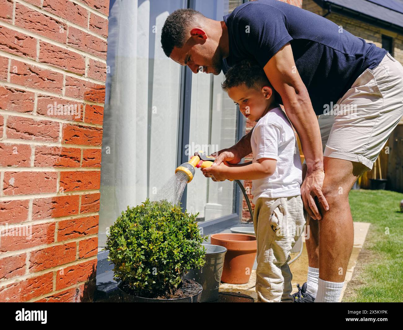 Father assisting son watering plant in back yard Stock Photo - Alamy
