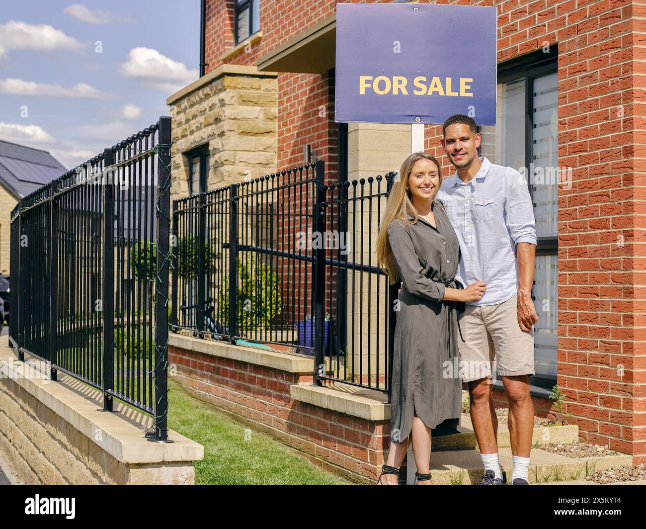 Smiling couple standing in front of house with For Sale sign Stock ...