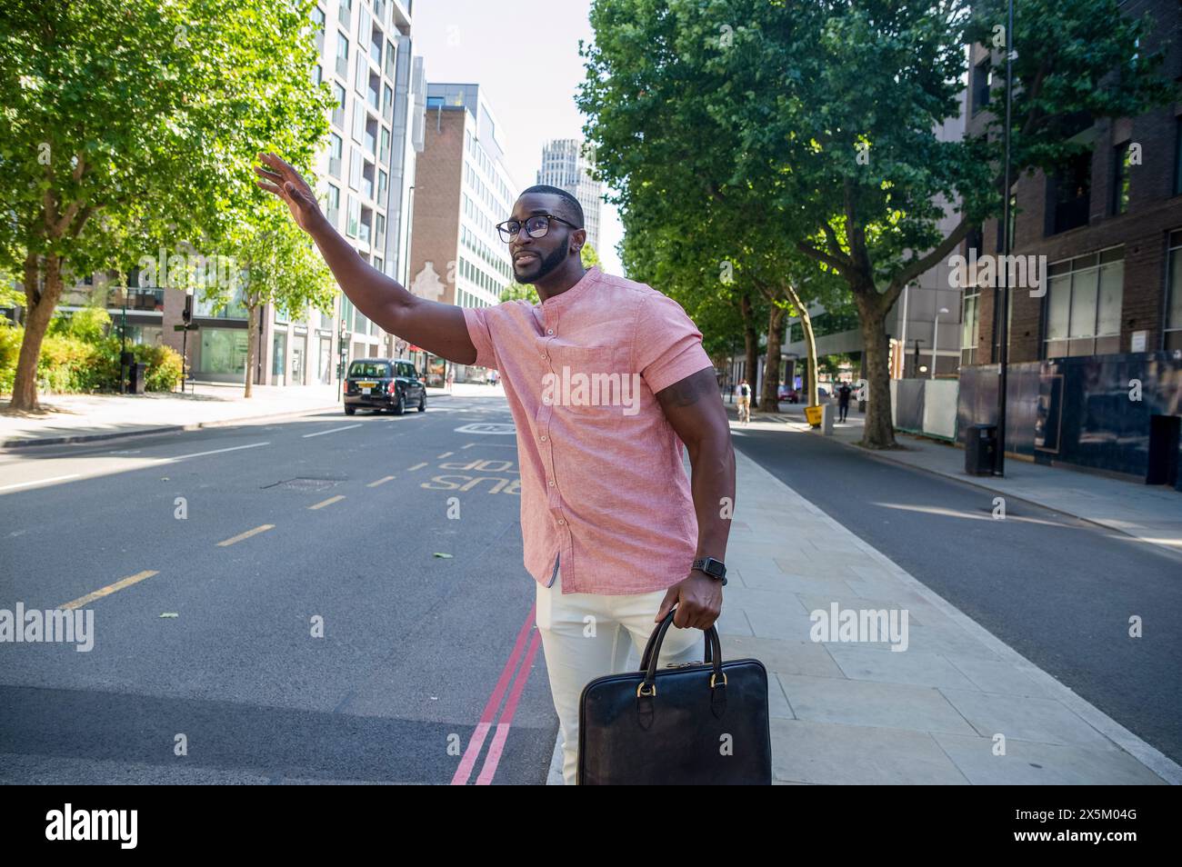 Man with briefcase standing on street and waving for transport Stock Photo