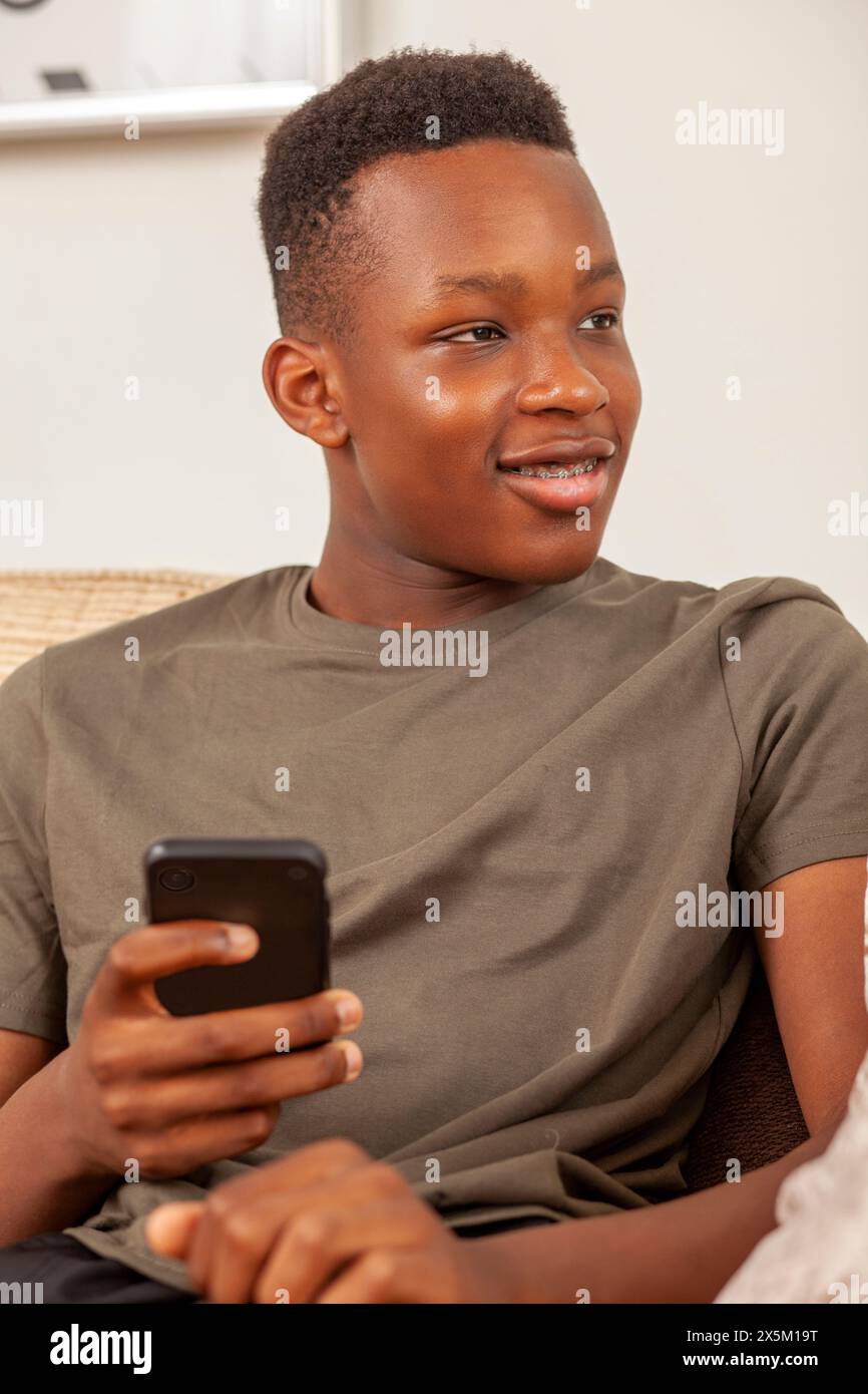 Teenage boy sitting on sofa and using phone Stock Photo