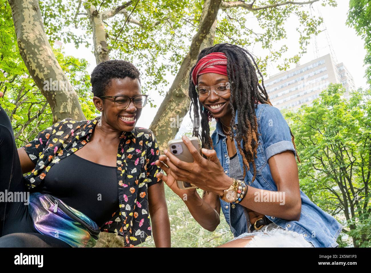 USA, Two smiling young women looking at smart phone in park Stock Photo