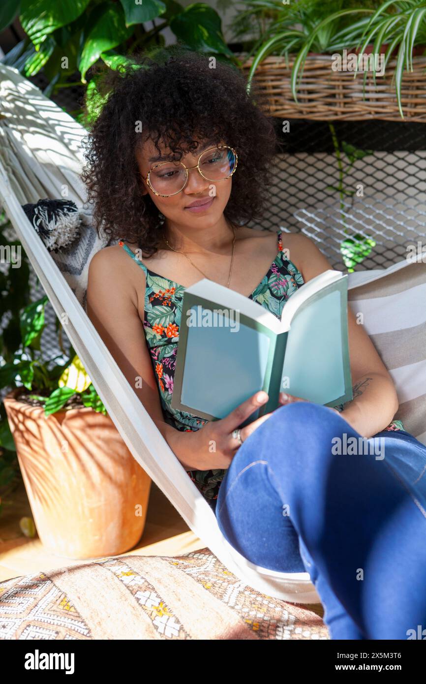 Woman sitting in hammock and reading book Stock Photo - Alamy