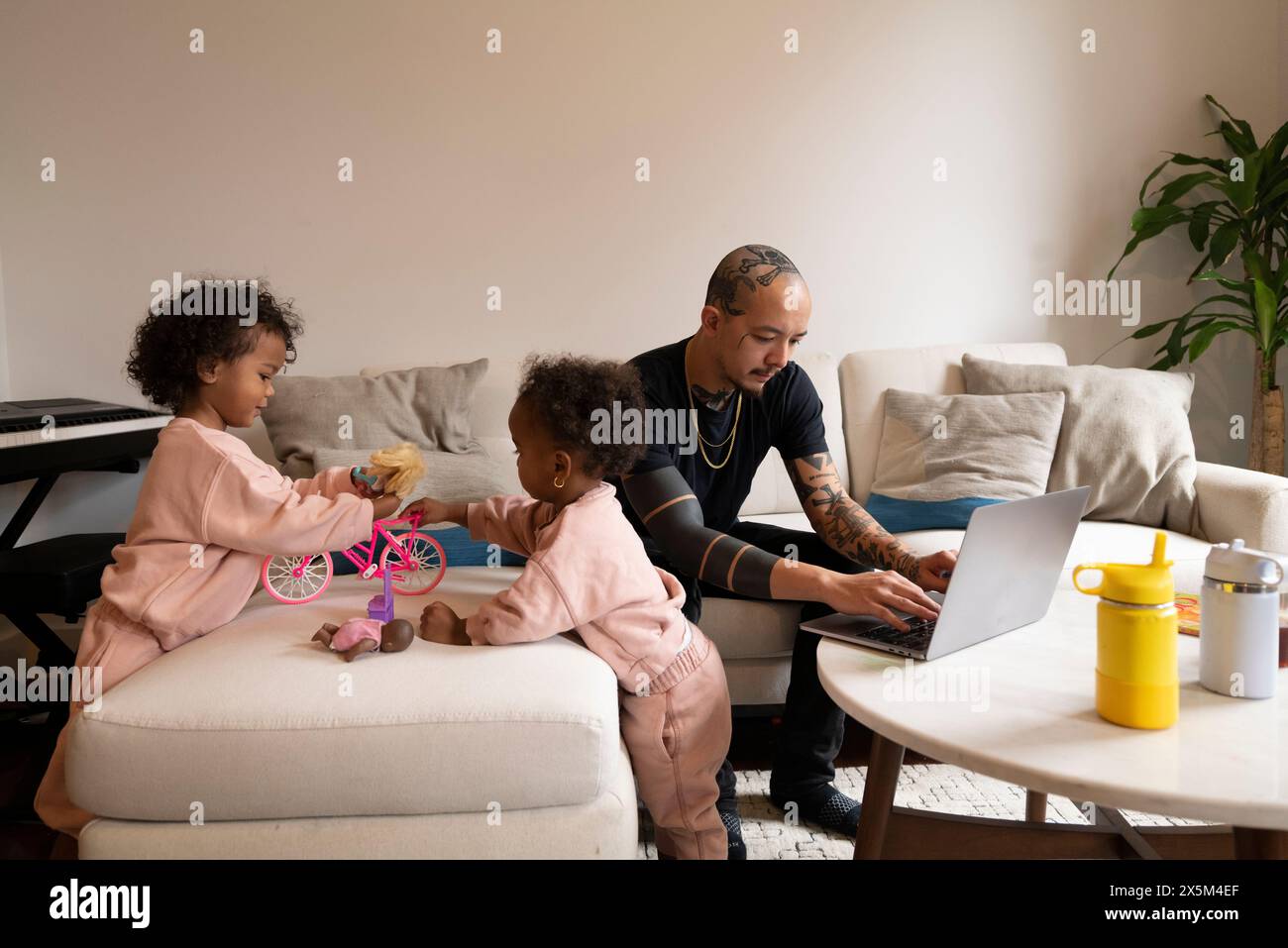 Father working on laptop while daughters playing Stock Photo