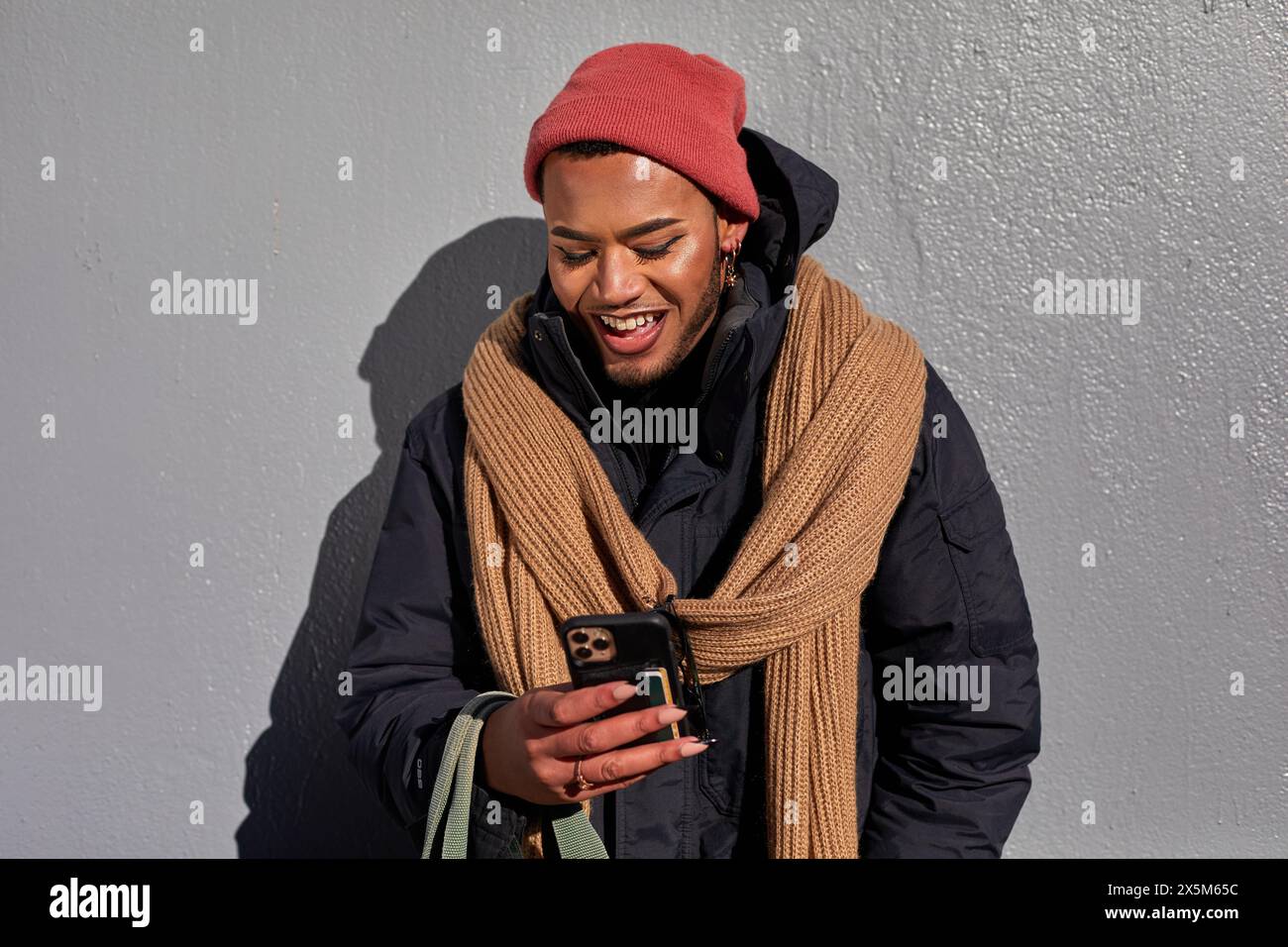 USA, New York City, Smiling queer man in warm clothing looking at smart phone Stock Photo