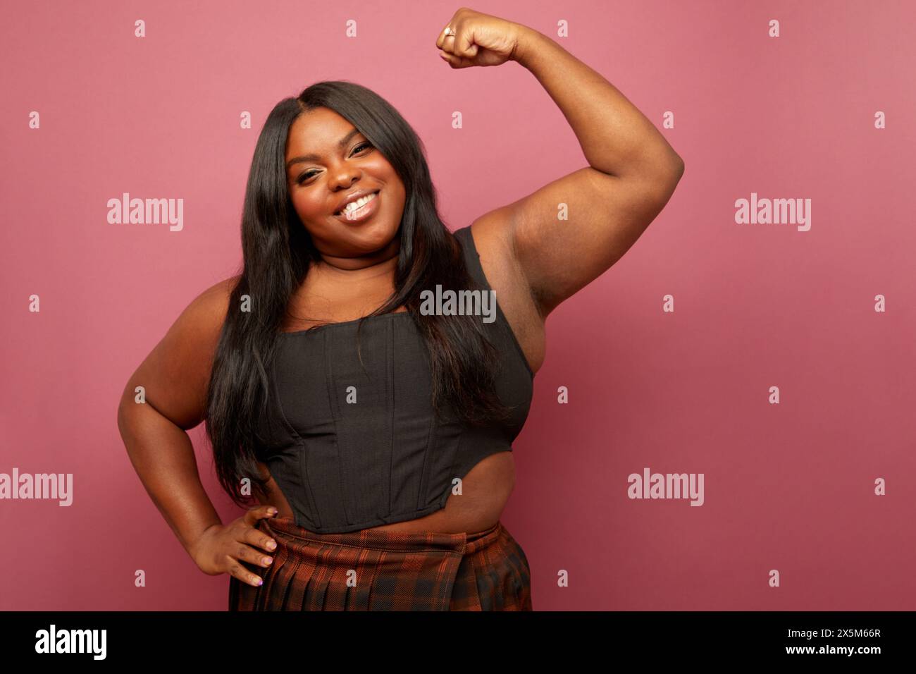 Studio portrait of woman flexing muscles against pink background Stock Photo