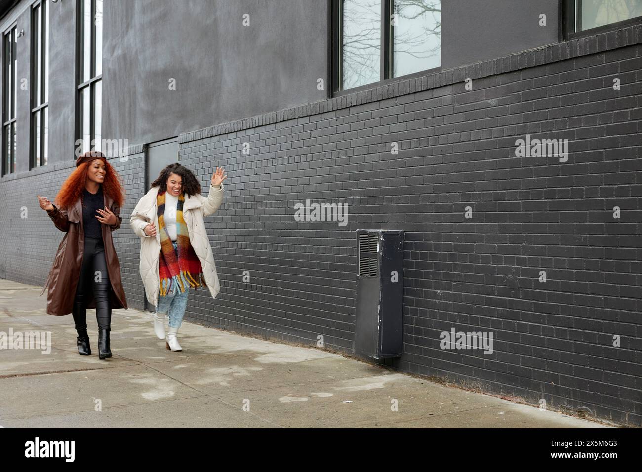 Smiling women walking alongside black building Stock Photo