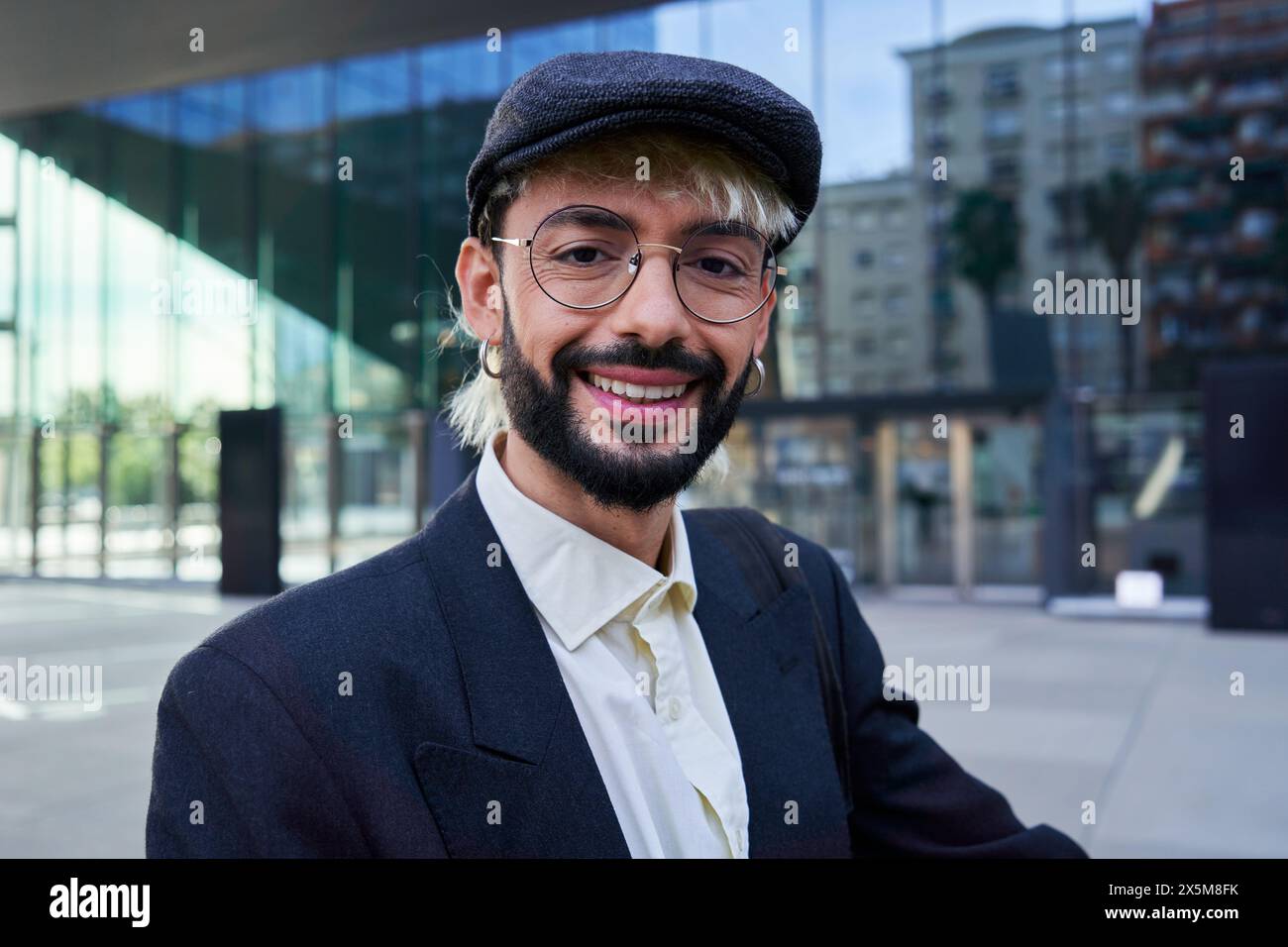 Hipster businessman looking at camera smiling, standing outside workplace. Stock Photo