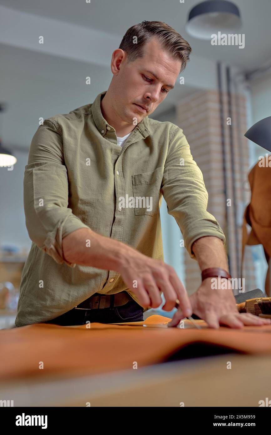 Close up side view hardworking artisan working with natural leather and tools. Handmade master at work in local workshop.blurred foreground Stock Photo