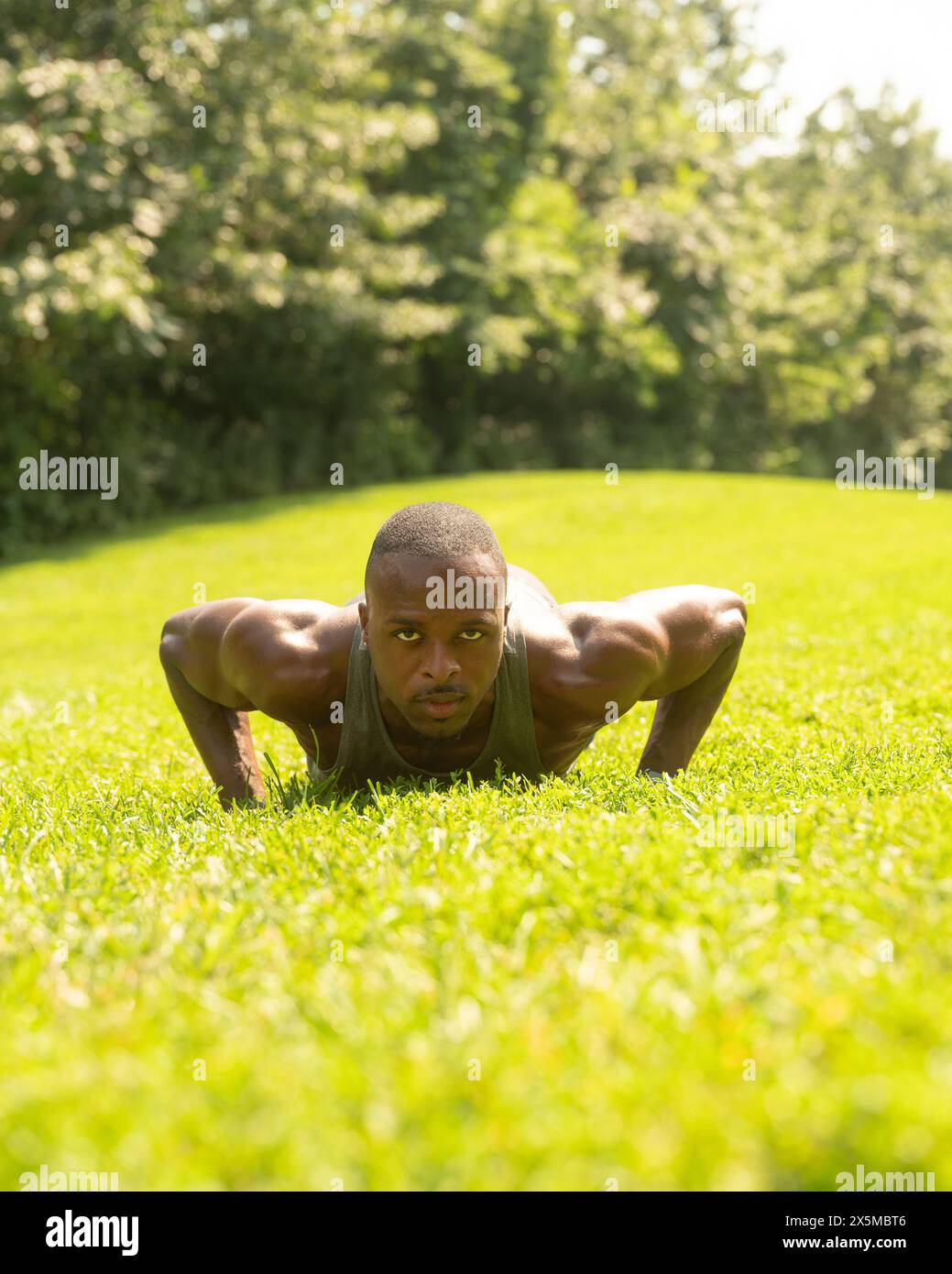 Athletic man doing push-ups on lawn in park Stock Photo
