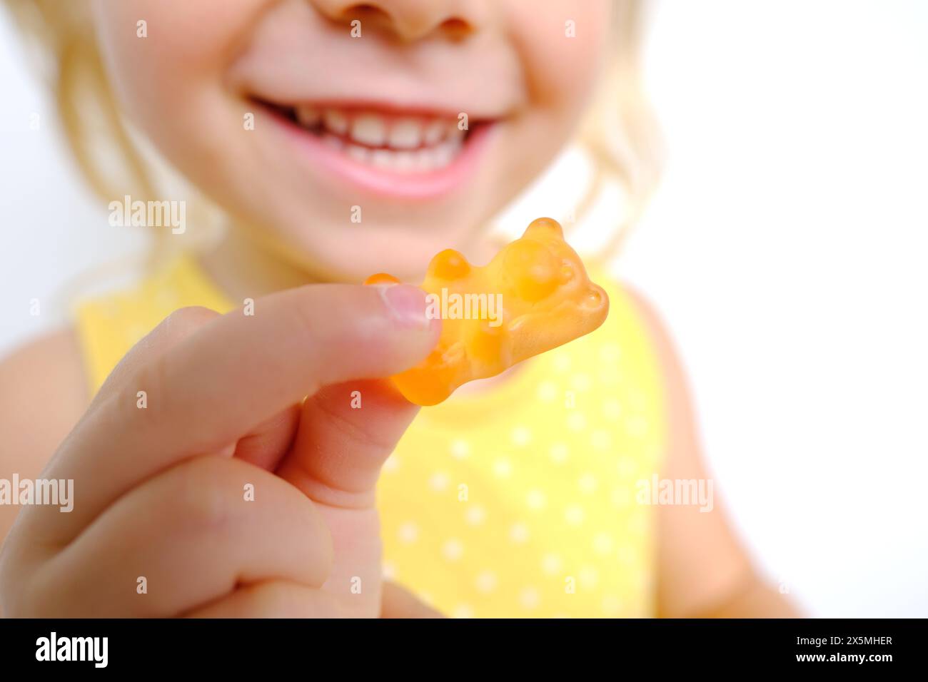 cheerful small child holds sweets, blonde girl 3 years old wants eat gelatinous candy with smile, gummy bear, kid has good appetite, happy childhood, Stock Photo
