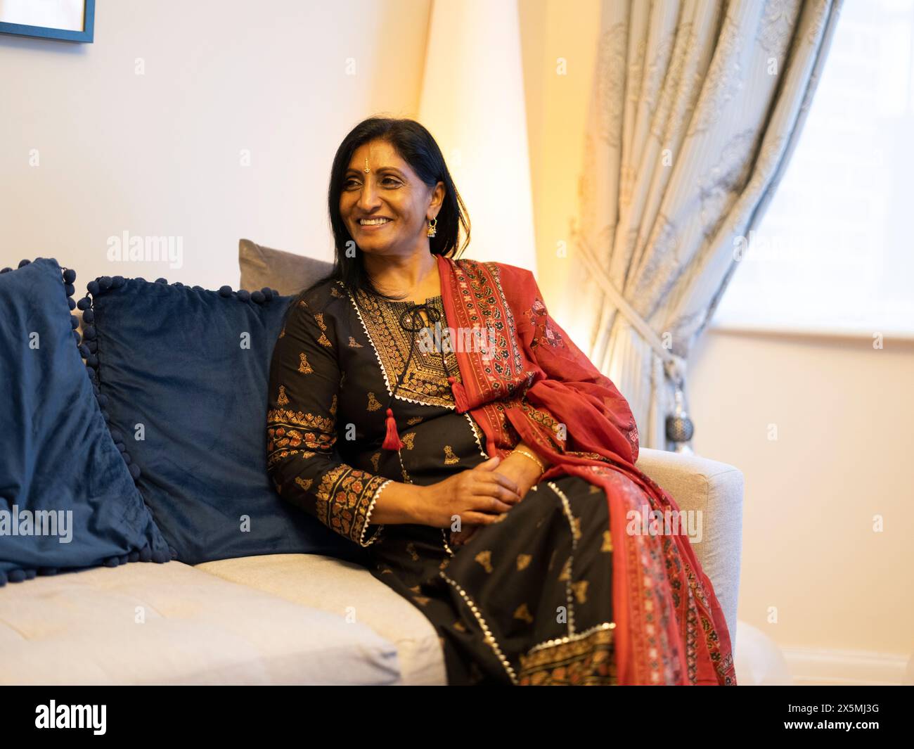 Smiling woman in traditional clothing sitting on sofa Stock Photo - Alamy