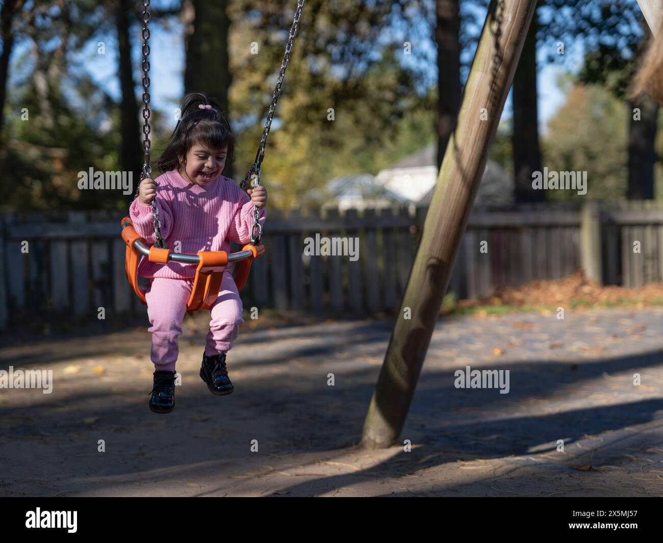 Girl with Down syndrome swinging on swing on playground Stock Photo