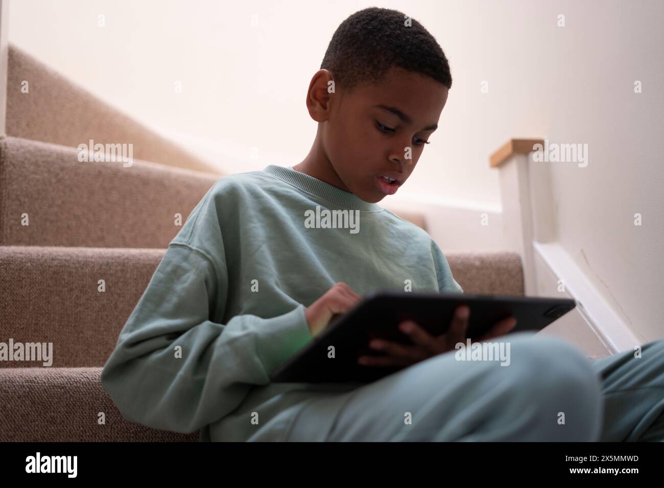 Boy sitting on stairs and using tablet Stock Photo - Alamy