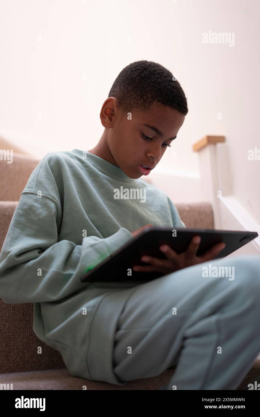 Boy sitting on stairs and using tablet Stock Photo - Alamy