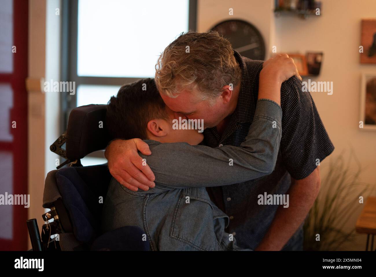 Father embracing disabled son at home Stock Photo