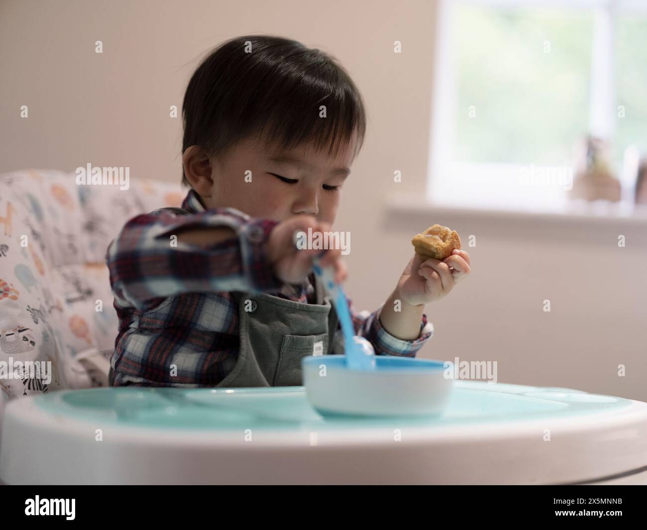 Baby boy sitting in high chair and eating Stock Photo