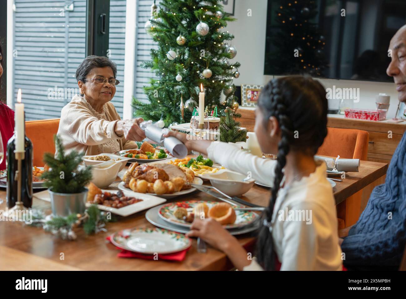 Girl with grandmother holding Christmas cracker across table Stock Photo