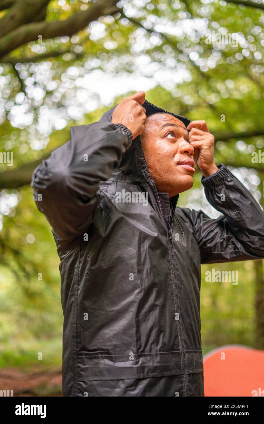Man putting on rain jackets hood in forest Stock Photo