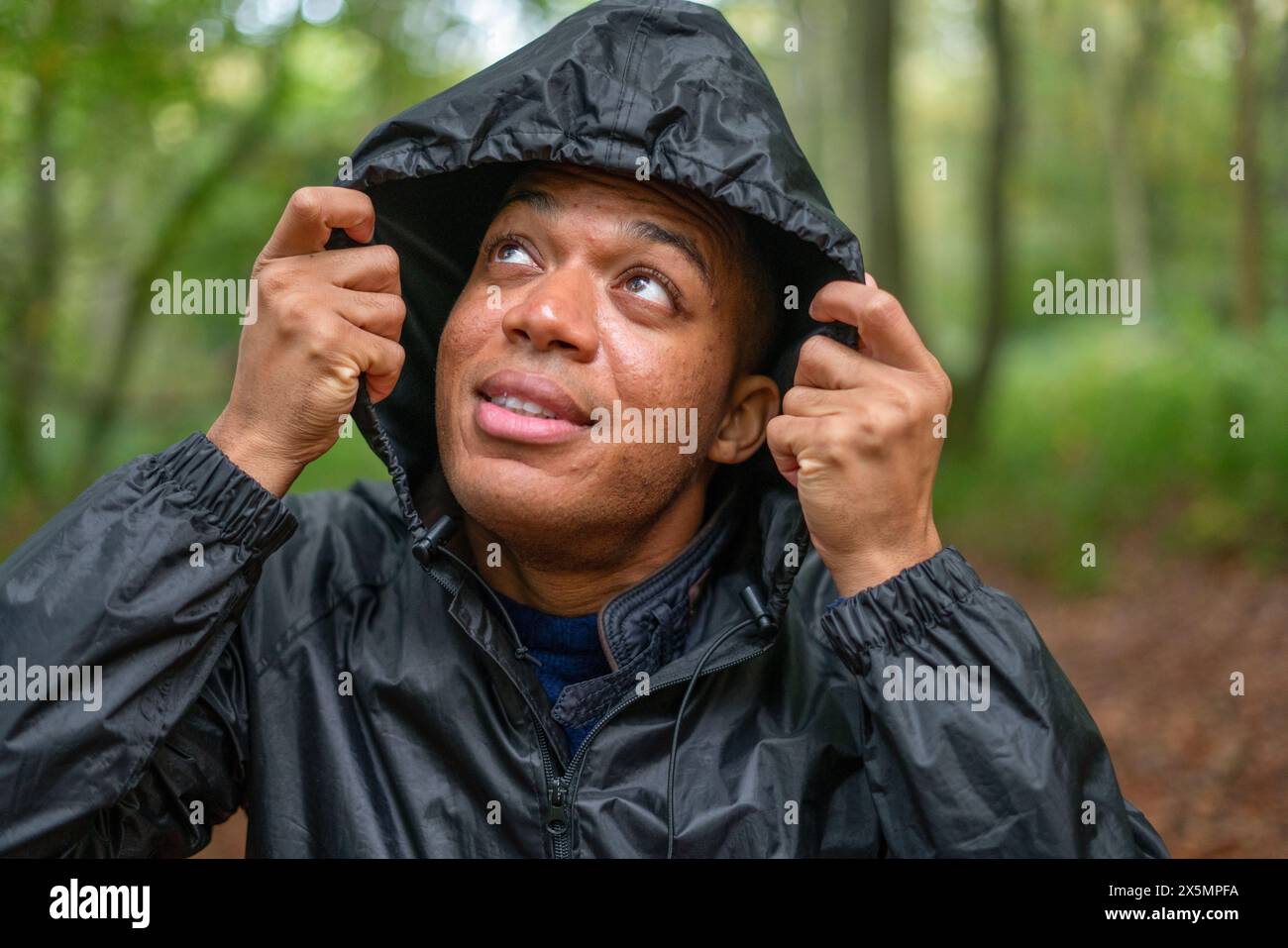 Man with rain jackets hood on looking up in forest Stock Photo