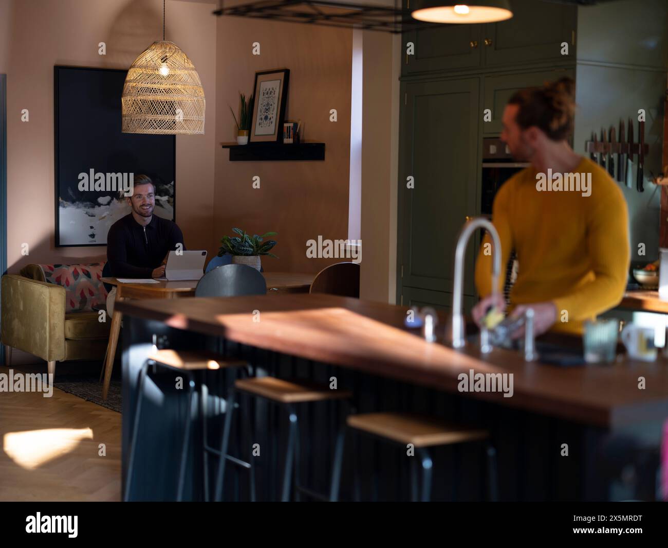 Man washing dishes while boyfriend using digital tablet at home kitchen Stock Photo