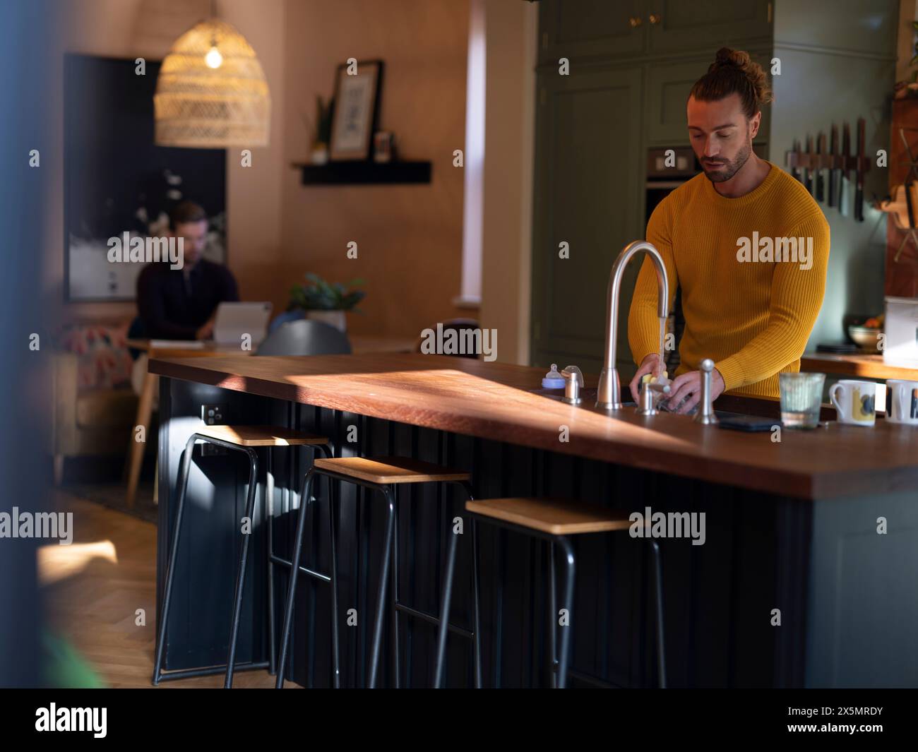 Man washing dishes while boyfriend using digital tablet at home kitchen Stock Photo