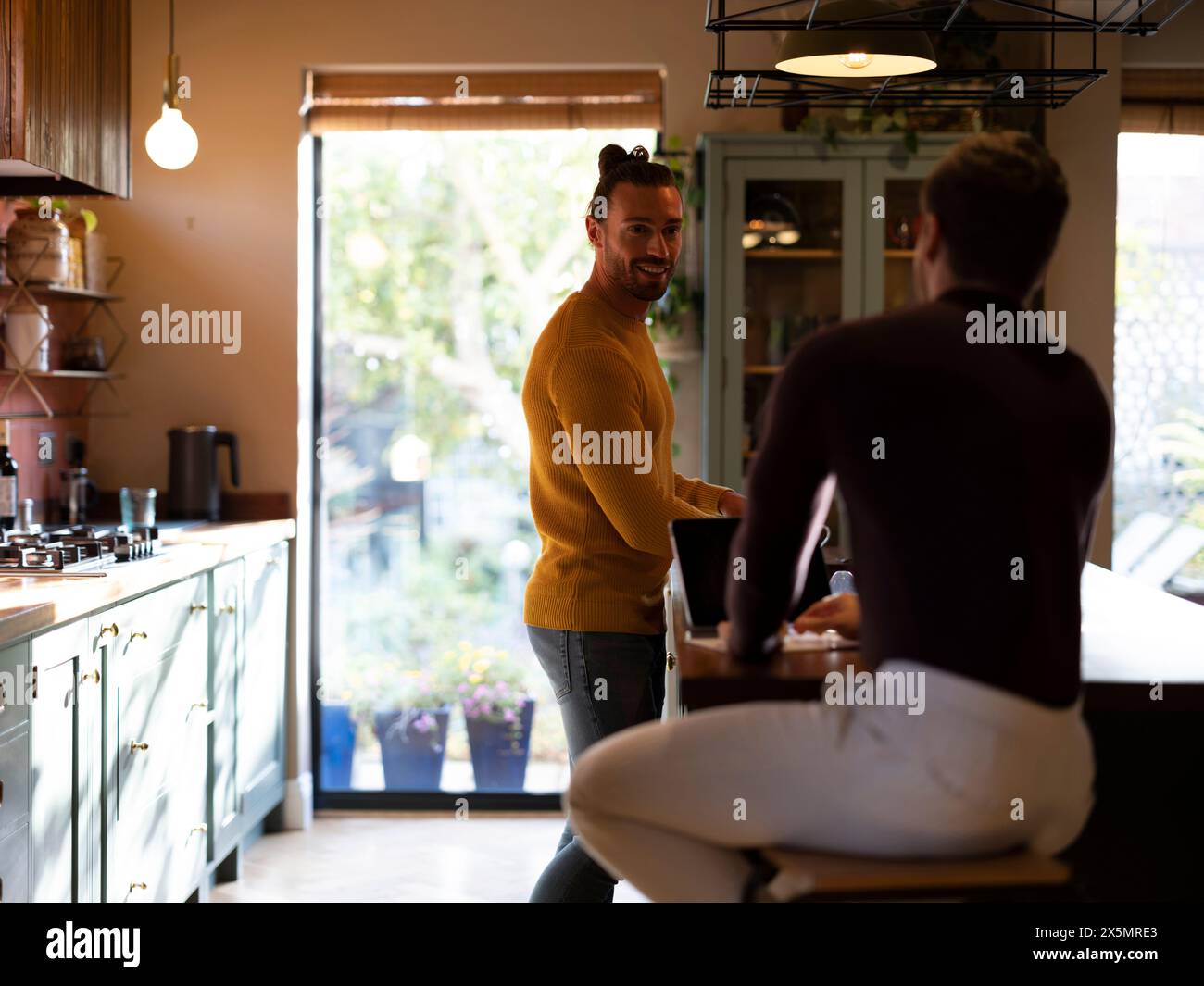 Man washing dishes while boyfriend using digital tablet at home kitchen Stock Photo