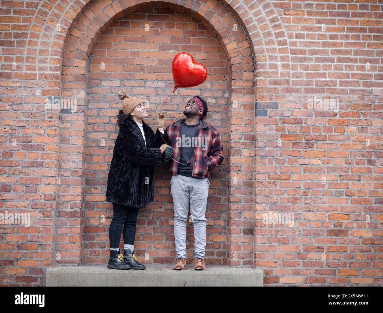 Couple with heart shaped balloon standing in brick wall niche Stock Photo