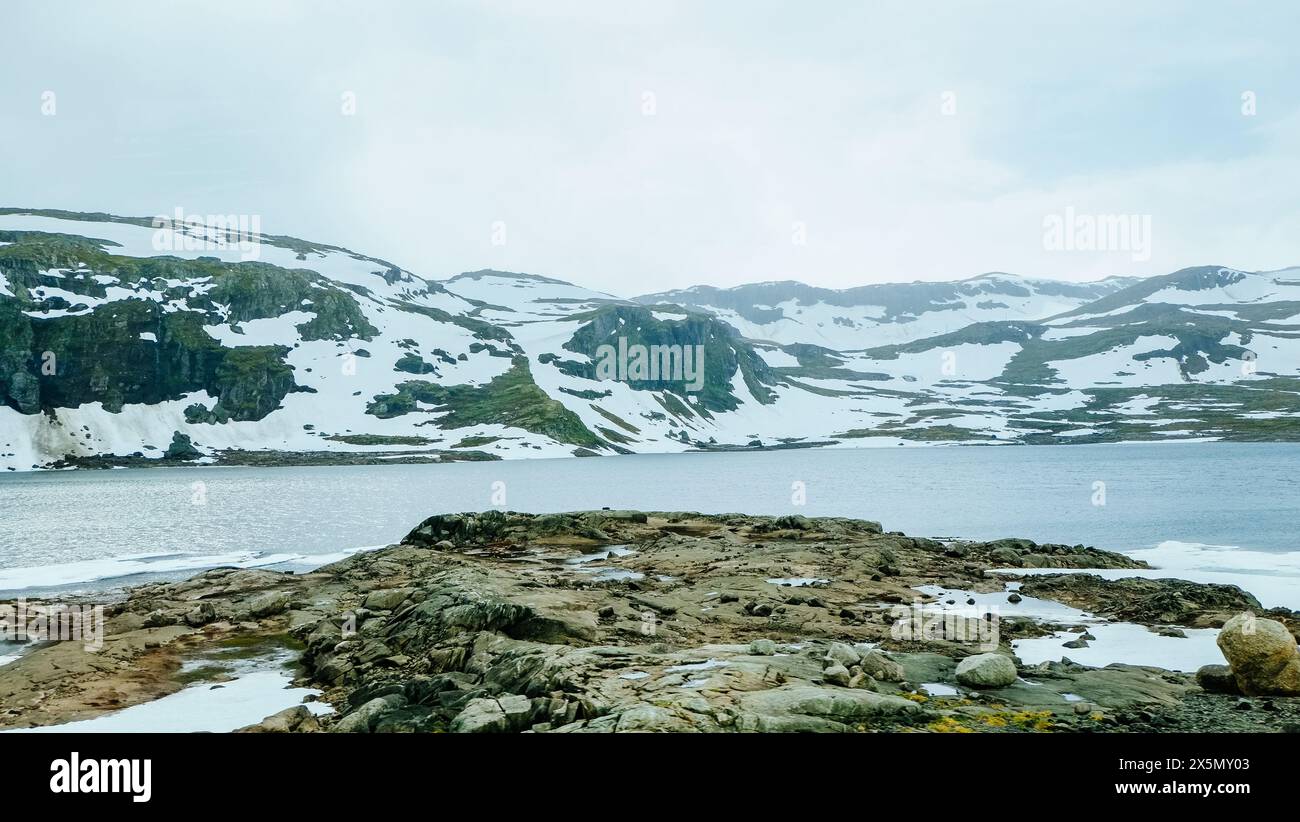 Winter nature landscape of snowcapped mountain hill and lake covered with ice snow in Norway countryside Stock Photo