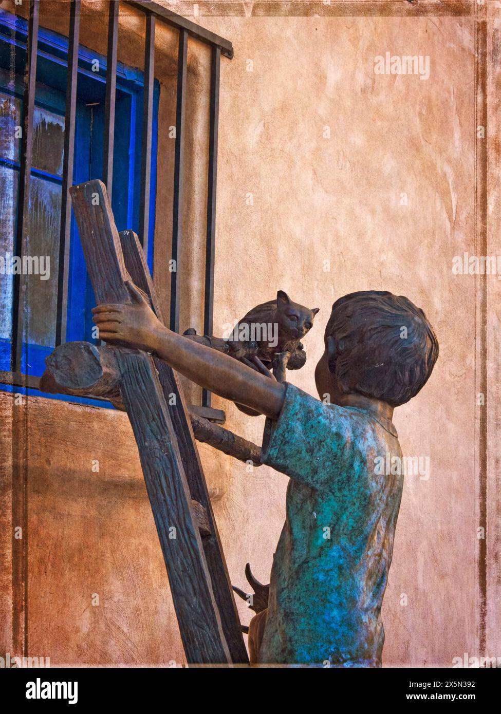 USA, New Mexico, Sante Fe. Colorful bronze statue of a boy on a ladder rescuing a cat from a window sill. (Editorial Use Only) Stock Photo