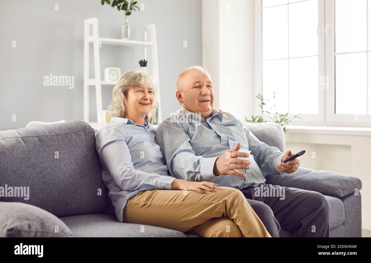 Senior couple watching football on tv holding TV remote and supporting sport team together. Stock Photo