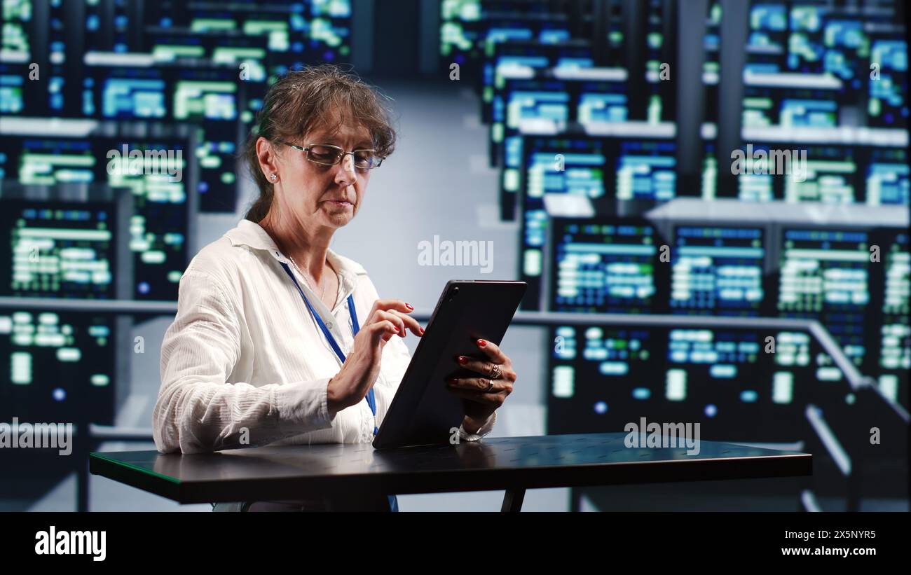 Precise serviceman in cloud computing company housing high end servers capable of quickly and efficiently performing complex computations and data analysis, using tablet to root out blips Stock Photo