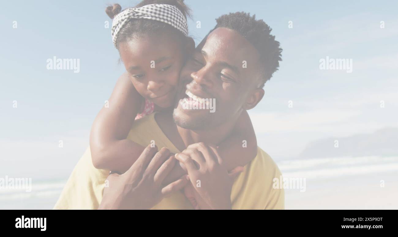 African American father holding young daughter, both smiling at beach Stock Photo