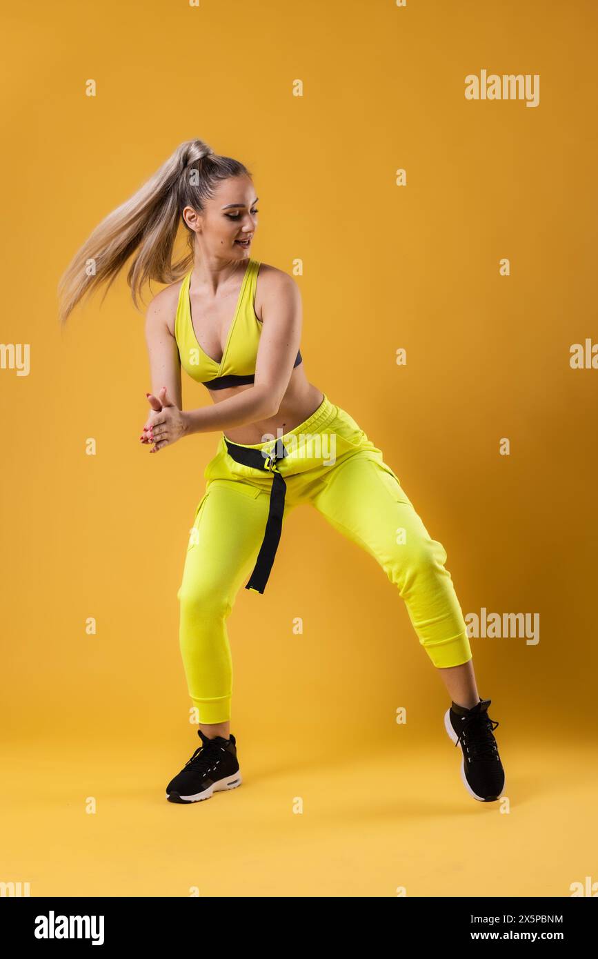 Beautiful girl in yellow outfit dancing zumba. Happy dance instructor against dark yellow or orange background. Stock Photo