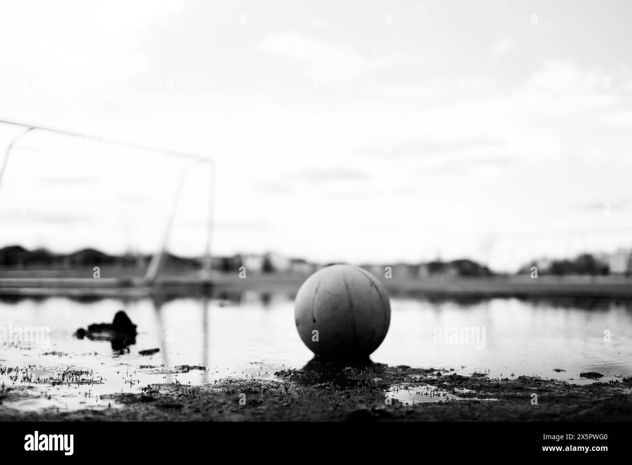 Selective focus on mud in front of a basketball sitting in a mudpuddle of water at a school playground.  Stock Photo
